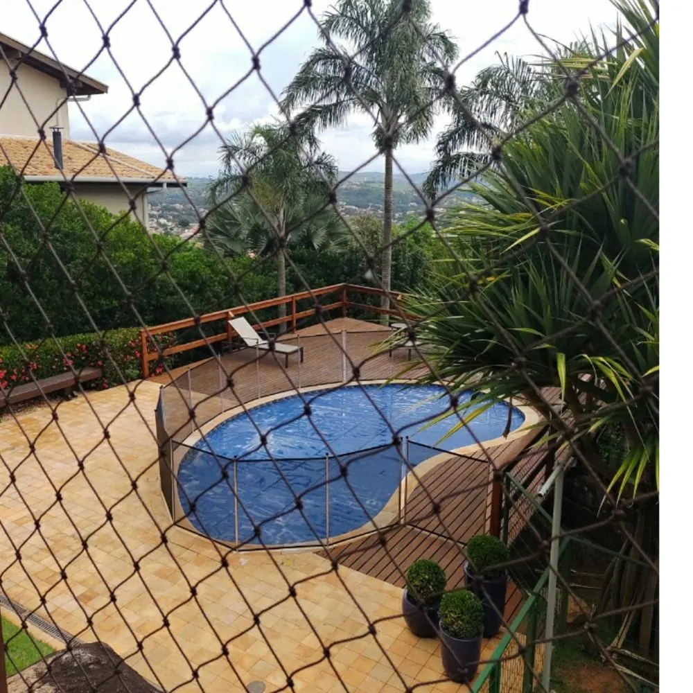 Vista da varanda protegida com rede sobre área de lazer com piscina e jardim