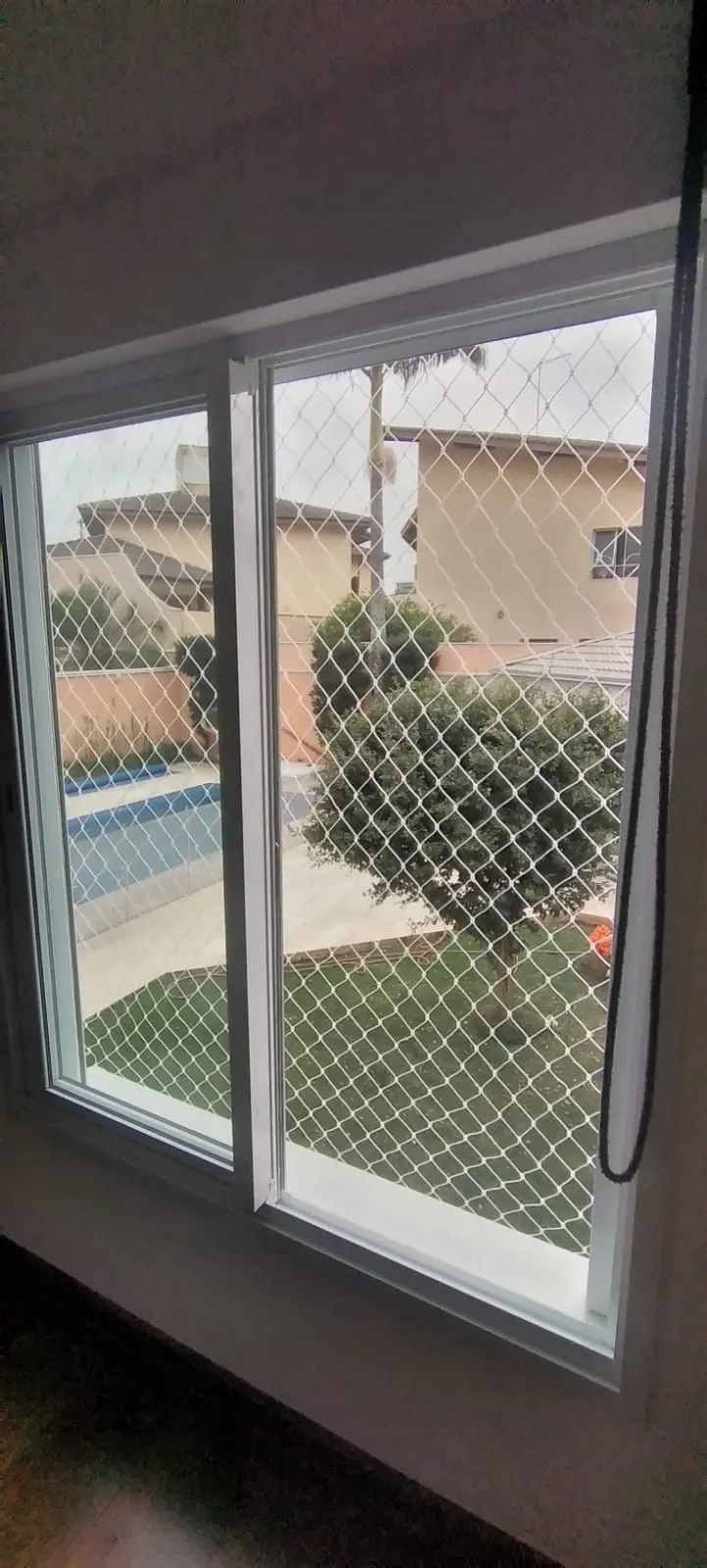Rede de proteção branca instalada em janela de residência com vista para a piscina